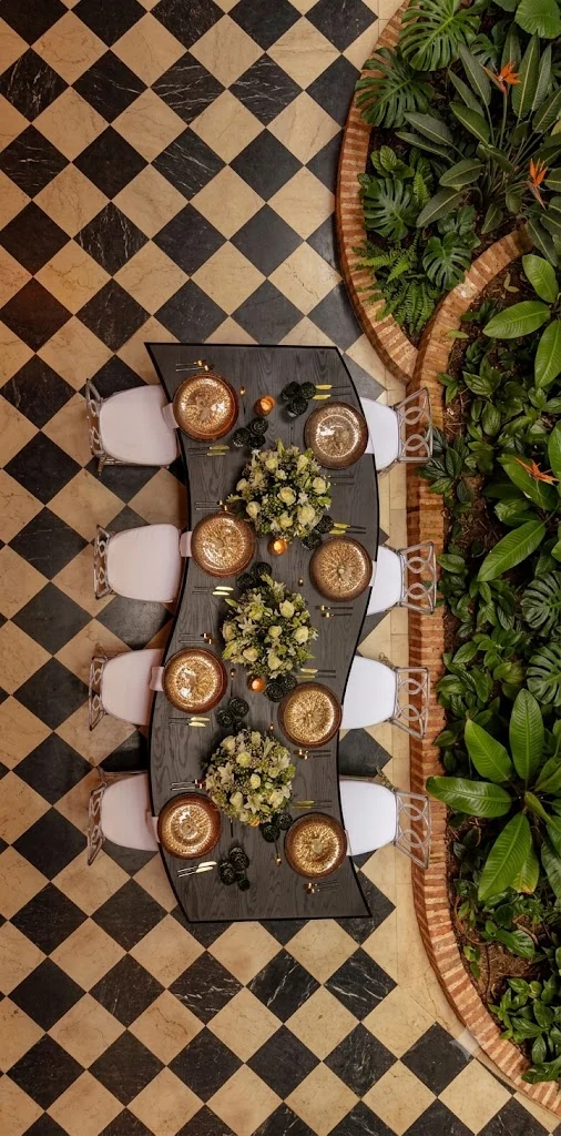 Mesa de madera oscura con platos dorados y follaje, vista desde arriba